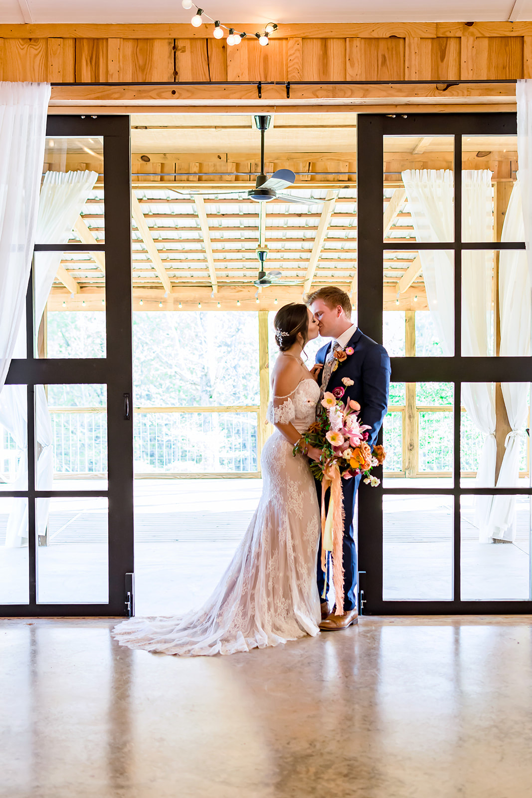 Bride and Groom kissing in front of modern glass doors at Georgia barn 
